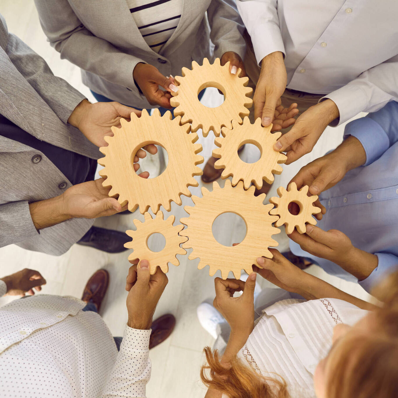 Wooden Gears Of Different Sizes Are In Hands Of Men And Women Who Connect Them To Pile. Wooden Gears Of Different Sizes Are In Hands Of Men And Women Who Connect Them To Pile.